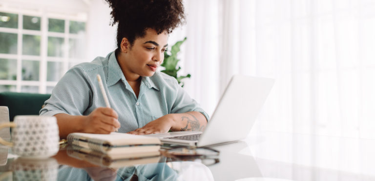 jovem mulher a ler artigo no computador e tirar notas sobre como melhorar o seu currículo